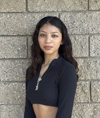 a young woman in a black crop top leaning against a brick wall