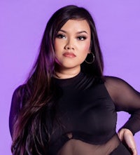 a woman in a black bodysuit posing on a purple background