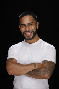 a man with tattoos and a white t - shirt smiling