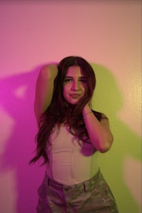 a young woman posing in front of a pink and purple wall